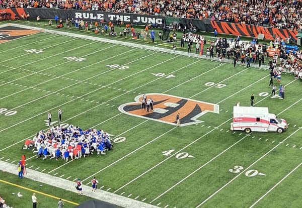 Damar Hamlin is removed from Paycor Stadium in an ambulance. The Buffalo Bills, in white, kneel in prayer at the bottom left of the image.